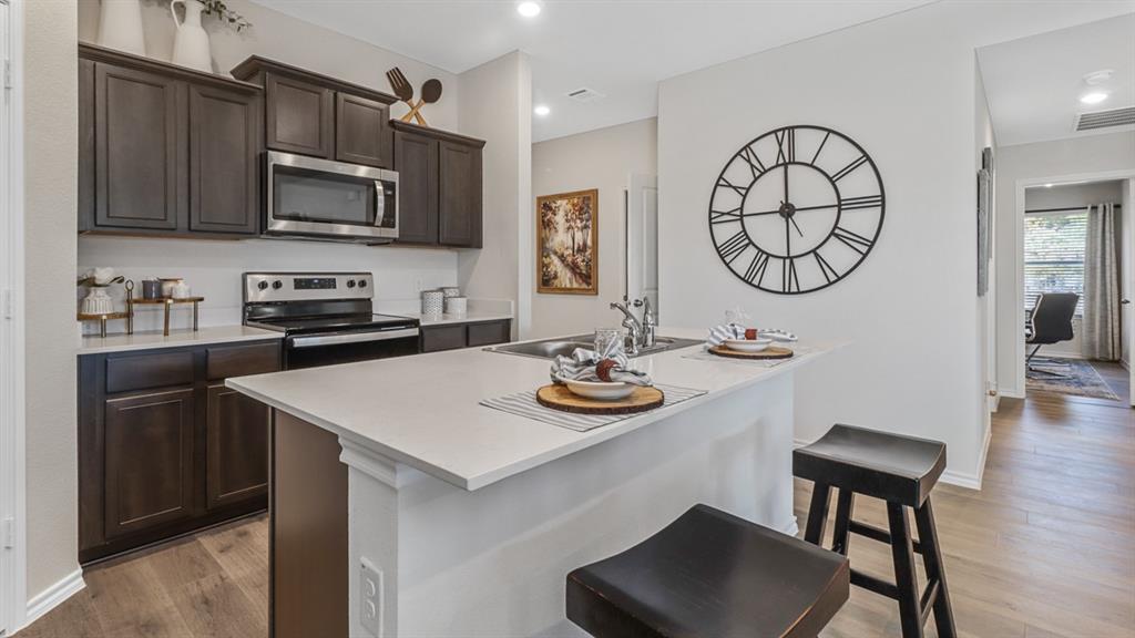 1667 Mantle Road Crandall, TX 75114 - Photo 5 of 20 Modern kitchen featuring dark wood-finish cabinetry, stainless steel appliances, a white tile backsplash, and a kitchen island with a light-toned countertop