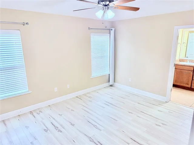 an empty room with wooden floor fan and windows