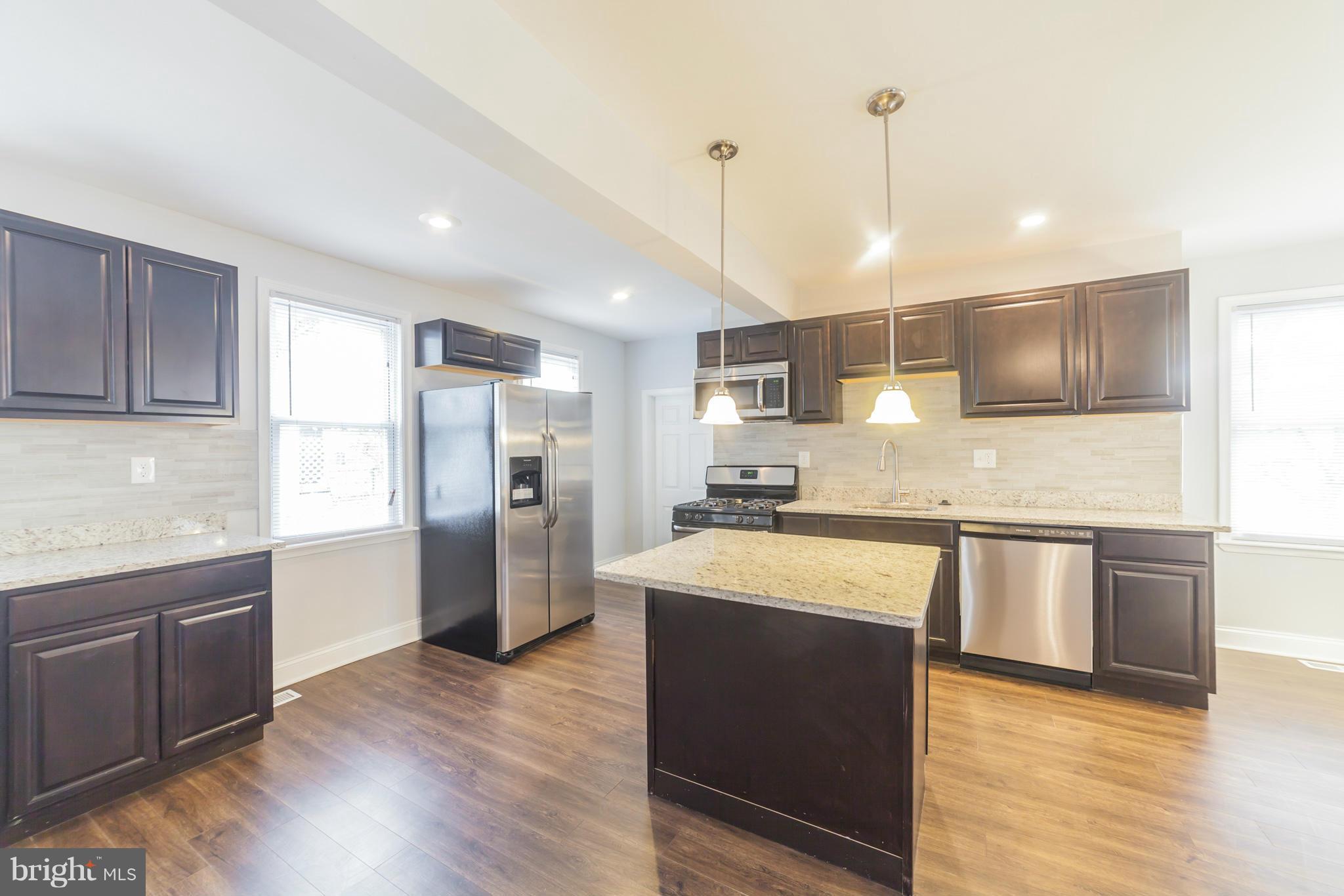 5502 Tramore Road Baltimore, MD 21214 - Photo 19 of 30 a large kitchen with stainless steel appliances granite countertop a sink a stove a refrigerator a center island and wooden floor