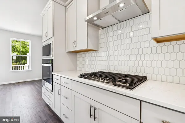 a kitchen with granite countertop a stove a sink dishwasher and white cabinets with wooden floor