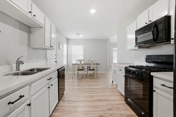 a kitchen with stainless steel appliances granite countertop a stove top oven a sink a dining table and chairs with wooden floor