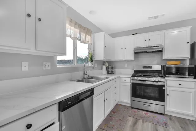 a kitchen with white cabinets appliances a sink and a window