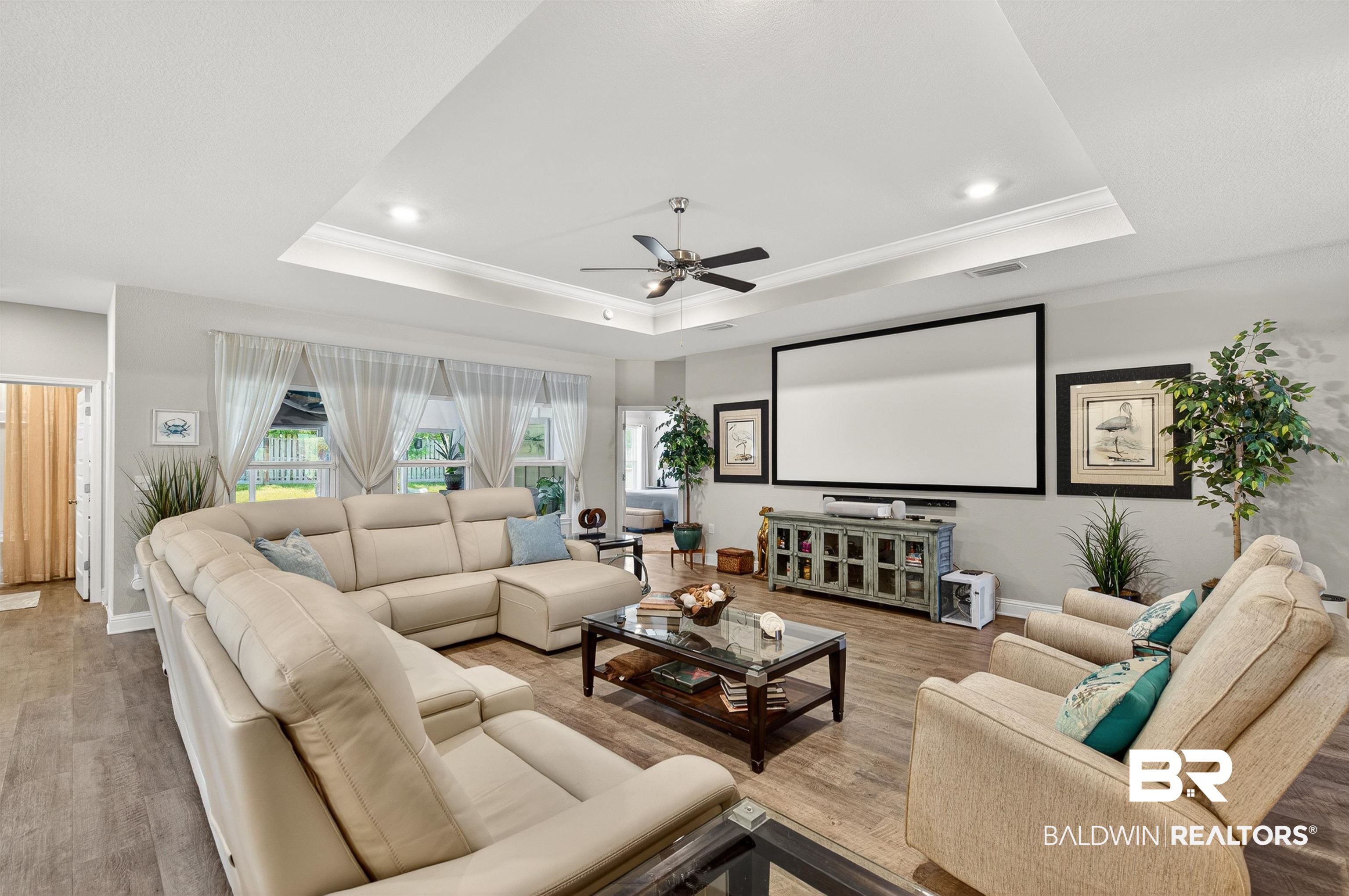 8735 Bronze Lane Foley, AL 36535 - Photo 5 of 58 Spacious living area featuring a tray ceiling with recessed lighting and a ceiling fan, wood-finish flooring, a large projection screen, and multiple windows with backyard views