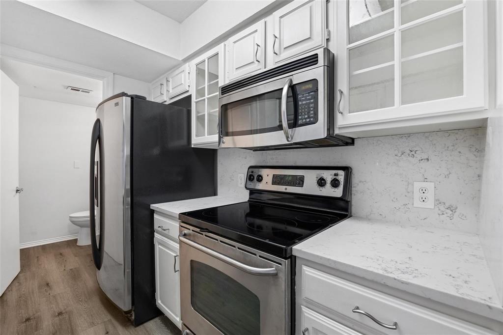 18240 Midway Road, Unit 402 Dallas, TX 75287 - Photo 9 of 29 Kitchen featuring white cabinetry, light-toned countertops, and a full suite of stainless steel appliances including a range and microwave
