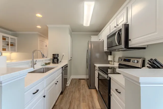 a kitchen with stainless steel appliances a sink stove oven a refrigerator with white cabinets and wooden floor