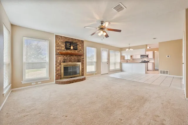 a view of a livingroom with a fireplace a ceiling fan and windows