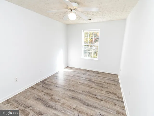 an empty room with wooden floor fan and windows