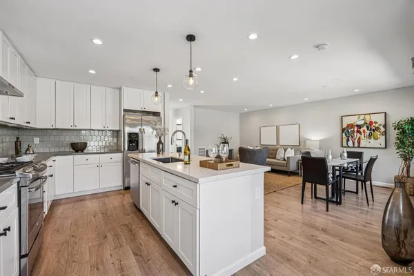 a kitchen with stainless steel appliances kitchen island granite countertop a stove top oven a sink a dining table and chairs with wooden floor