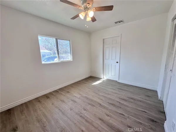 an empty room with wooden floor chandelier fan and windows