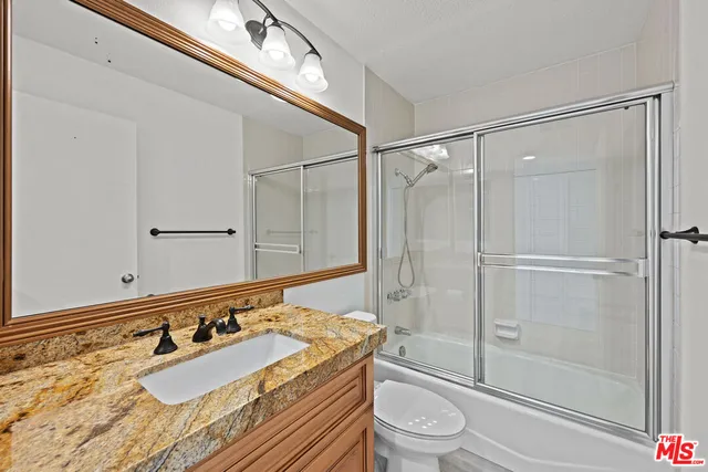 a bathroom with a granite countertop sink a toilet and shower