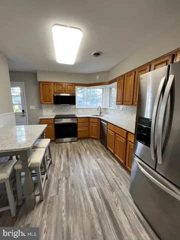 a kitchen with stainless steel appliances granite countertop a refrigerator a sink dishwasher a stove and white countertops with wooden floor