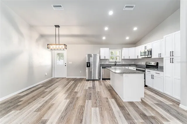 a kitchen with stainless steel appliances granite countertop a refrigerator a sink dishwasher a stove top oven a refrigerator and white cabinets with wooden floor