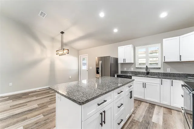 a kitchen with stainless steel appliances granite countertop a refrigerator a oven and white cabinets with wooden floor