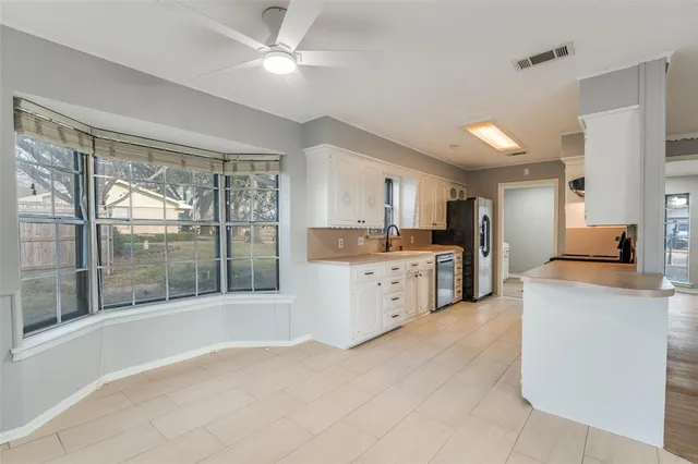 a kitchen with stainless steel appliances kitchen island granite countertop a refrigerator a sink and white cabinets with wooden floors