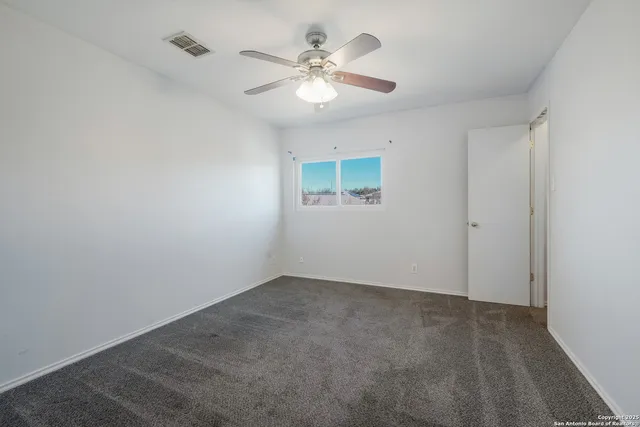 an empty room with a chandelier fan and windows