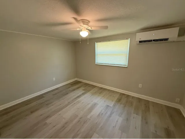 a view of an empty room with wooden floor and a chandelier fan