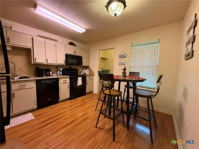 a kitchen with stainless steel appliances granite countertop a stove top oven a sink dishwasher a dining table and chairs with wooden floor