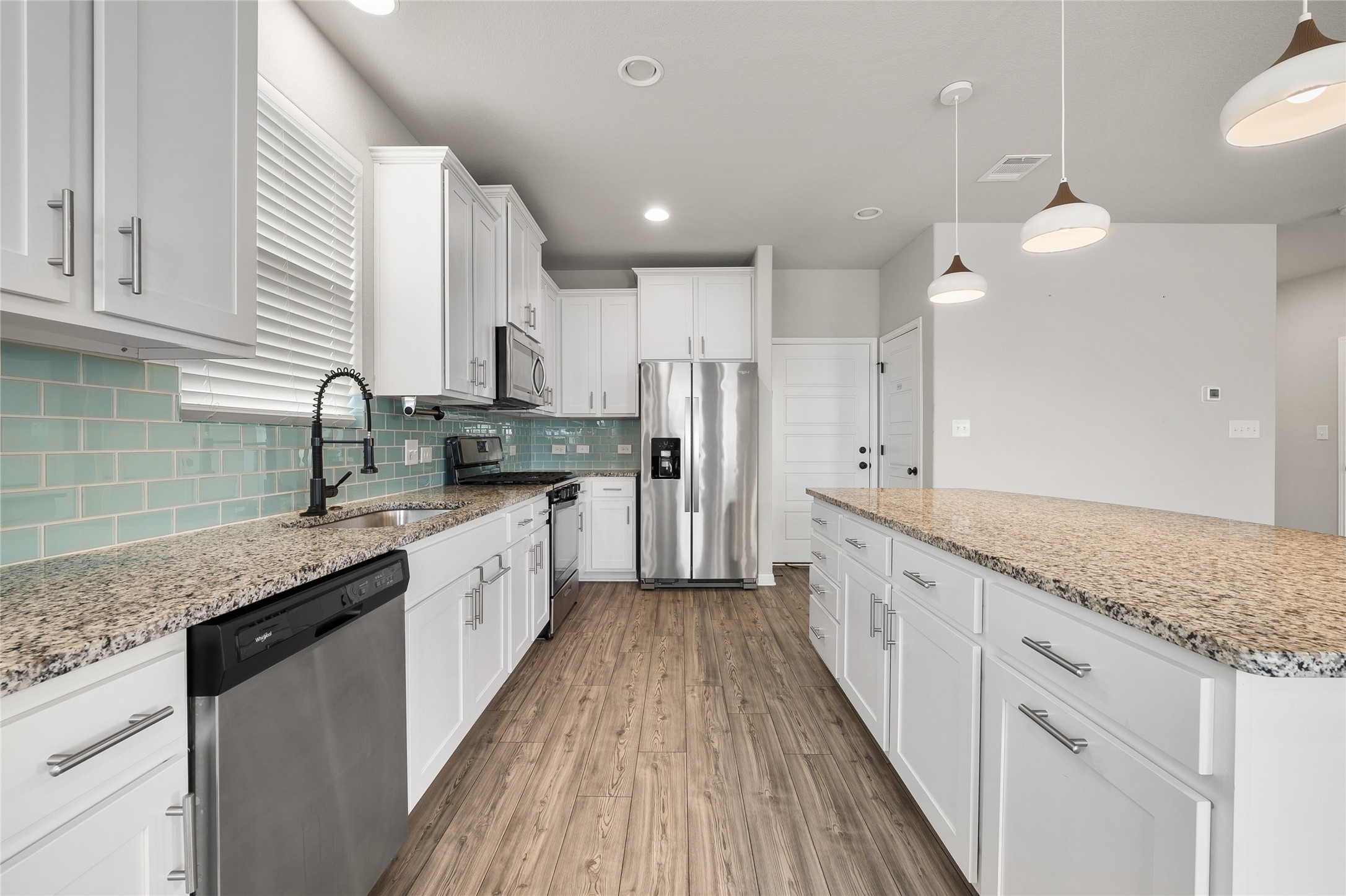 101 Lambert Street Leander, TX 78641 - Photo 13 of 33 An inviting kitchen with pristine white cabinetry, granite countertops, and modern pendant lighting over a spacious island.