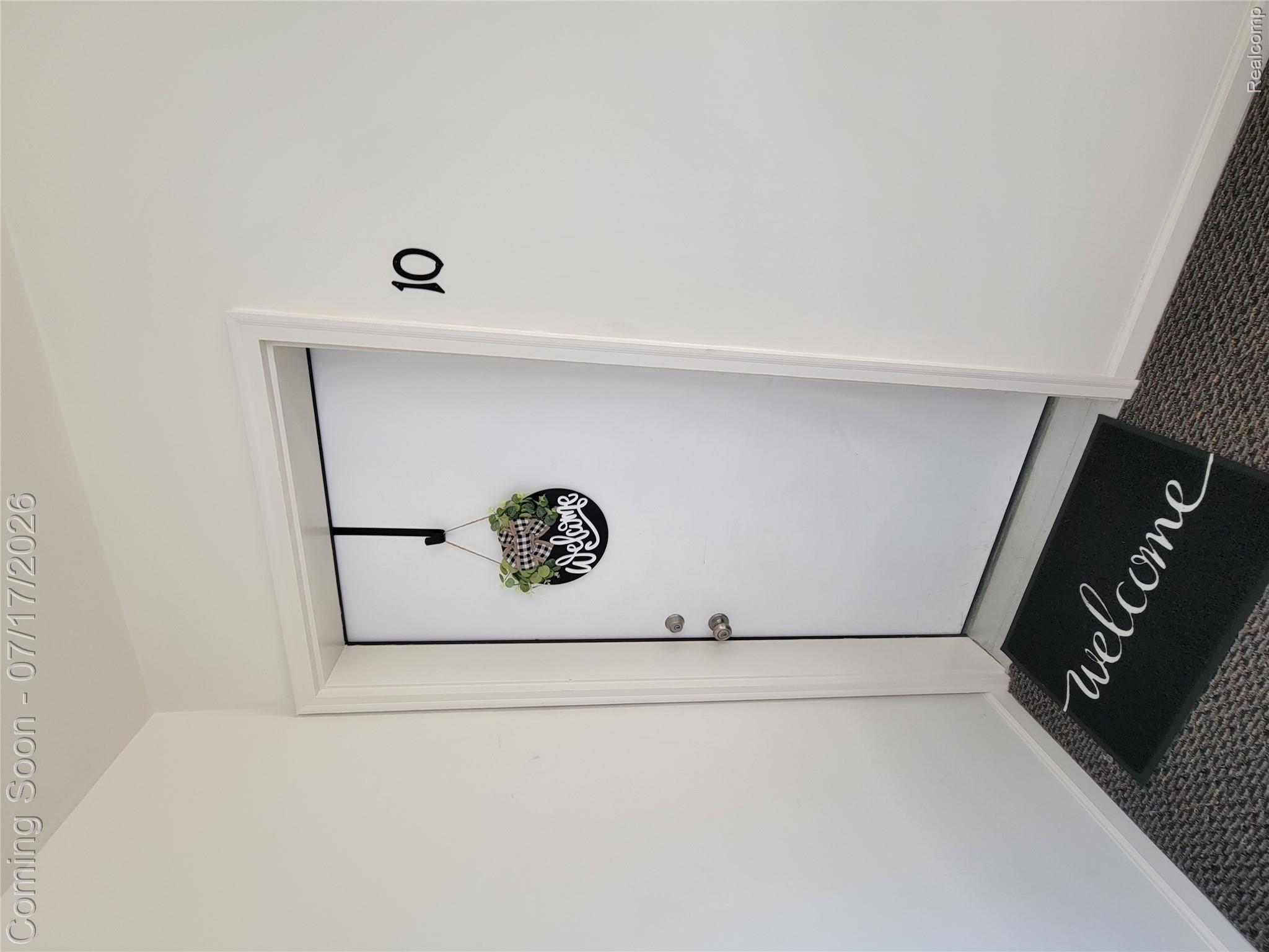 White entry door with polished chrome hardware, black numbering, and dark gray flooring