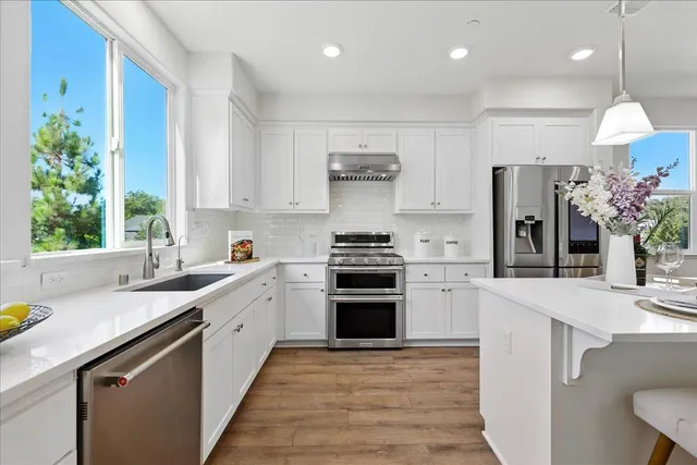 a kitchen with stainless steel appliances granite countertop a refrigerator a oven a sink a dining table and chairs with wooden floor