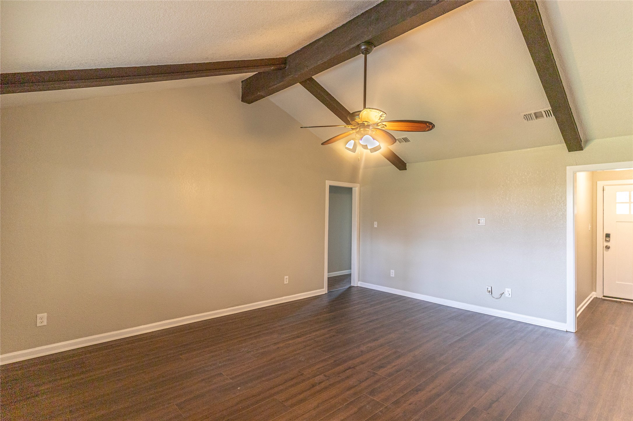 14419 Wadebridge Way Houston, TX 77015 - Photo 9 of 20 The room features a vaulted ceiling with exposed wooden beams and a ceiling fan. It has a warm, neutral color palette and wood-look flooring, providing a spacious and inviting atmosphere.