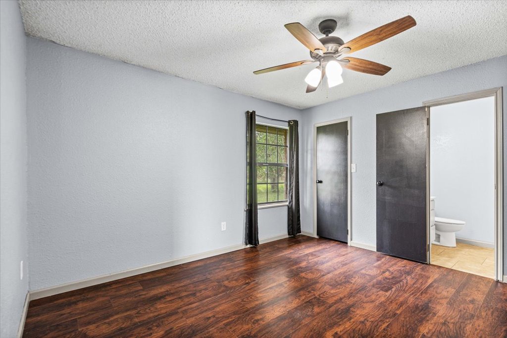 650 West Austin Street Luling, TX 78648 - Photo 11 of 18 Rich hardwood floors complement a bedroom with a view of mature outdoor foliage, illuminated by an overhead ceiling fan.