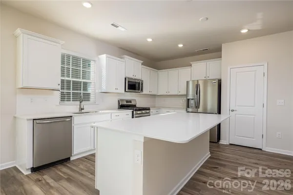 a kitchen with stainless steel appliances granite countertop a sink a stove a refrigerator with white cabinets and wooden floor