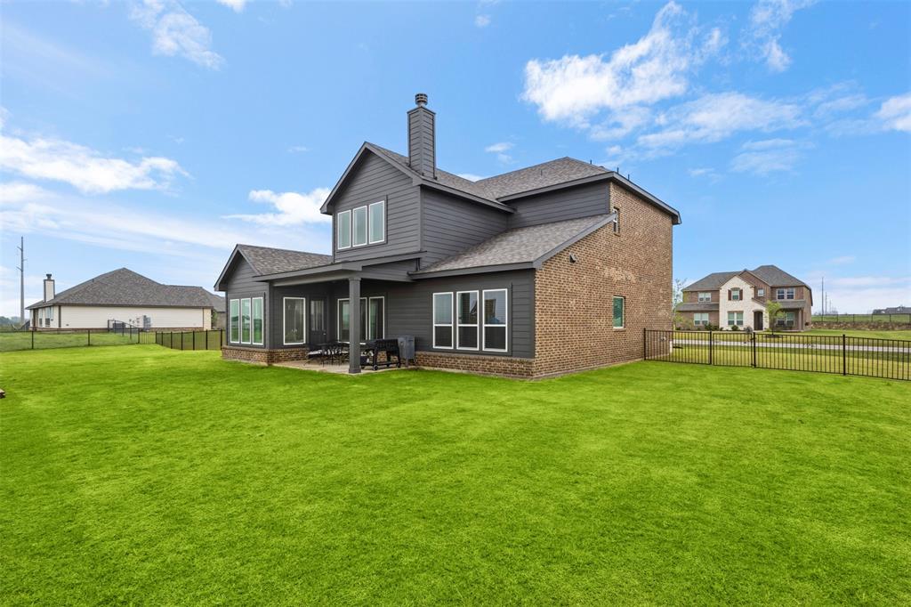 107 Yampa Court Rhome, TX 76078 - Photo 26 of 30 Expansive green lawn with a covered patio, featuring a brick and dark siding exterior, multiple windows, and a black metal fence