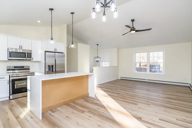 a kitchen with stainless steel appliances granite countertop a refrigerator a sink dishwasher a stove and white cabinets with wooden floor