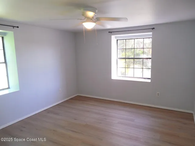 an empty room with wooden floor fan and windows
