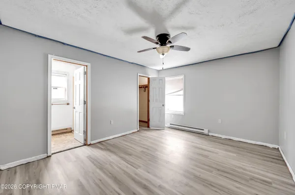 a view of an empty room with wooden floor and a ceiling fan