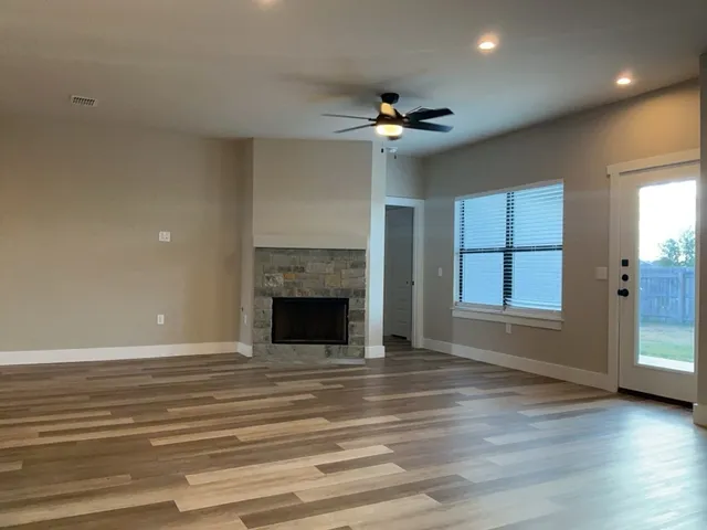 an empty room with wooden floor fireplace and windows