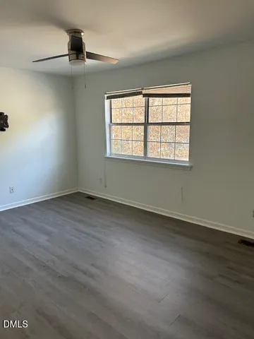 an empty room with wooden floor fan and windows