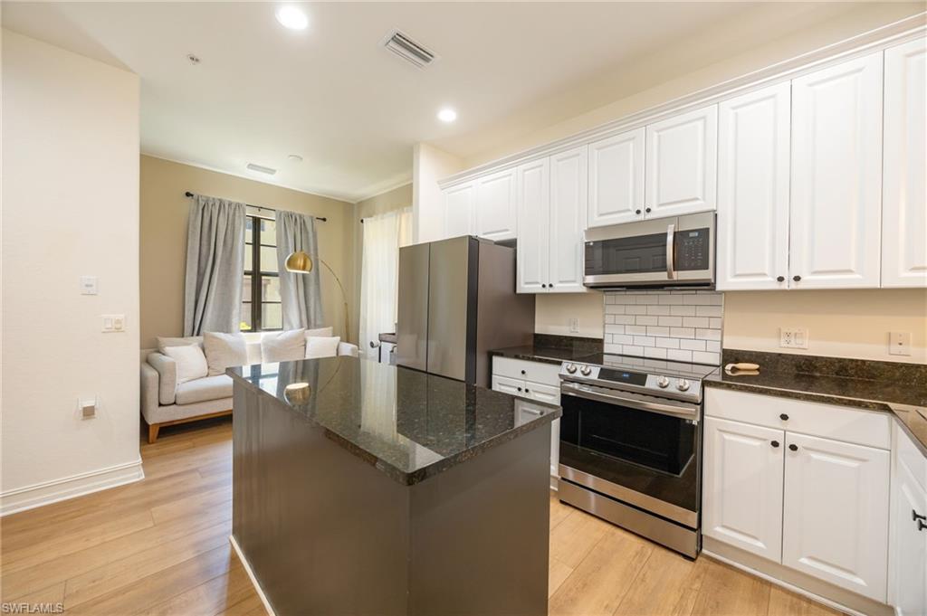 a kitchen with stainless steel appliances granite countertop a stove a sink dishwasher a refrigerator and a microwave oven with white cabinets