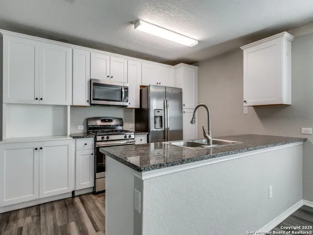 a kitchen with stainless steel appliances granite countertop a stove a sink dishwasher a refrigerator and white cabinets with wooden floor