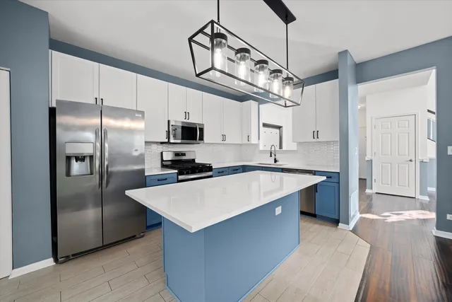 a large kitchen with stainless steel appliances kitchen island granite countertop a refrigerator a sink dishwasher a stove and a refrigerator with wooden floor