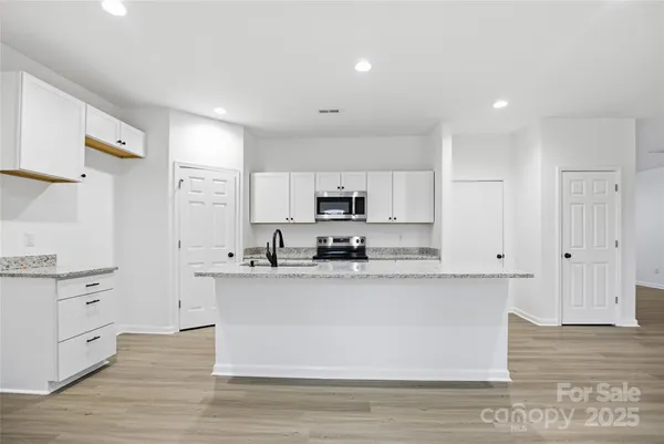 a large kitchen with stainless steel appliances granite countertop a stove top oven a sink a refrigerator and white cabinets with wooden floor