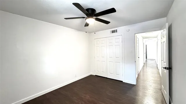 an empty room with wooden floor ceiling fan and windows