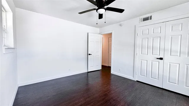 an empty room with wooden floor fan and windows