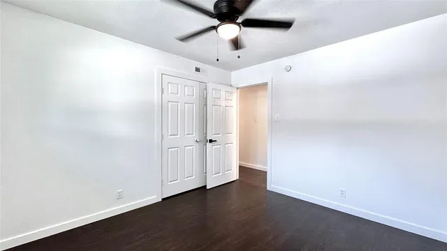 an empty room with wooden floor fan and windows