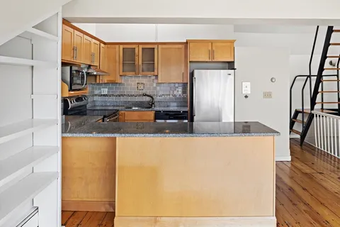 a kitchen with granite countertop a refrigerator a sink and wooden floors