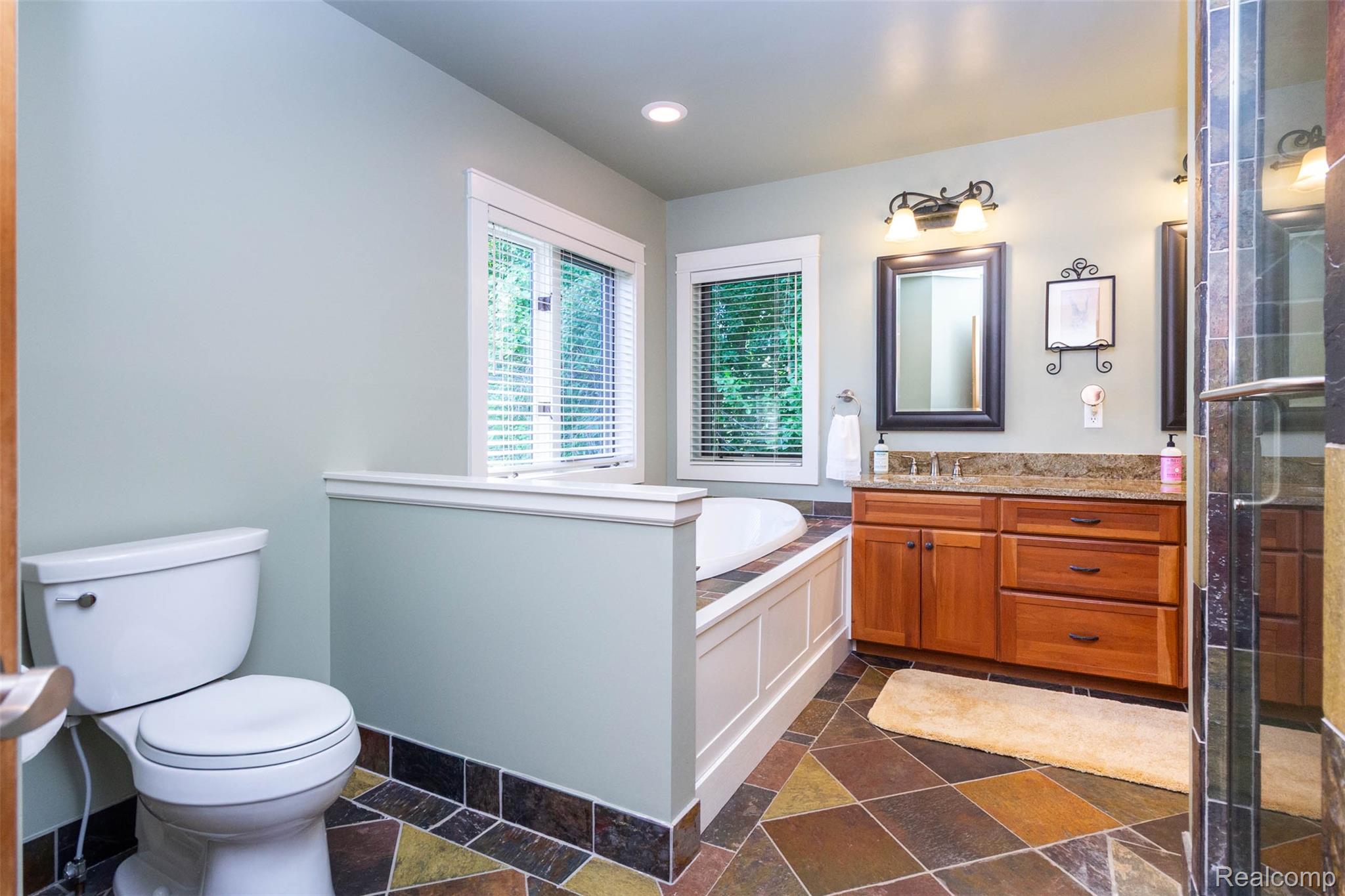 9887 Hadley Road Clarkston, MI 48348 - Photo 20 of 56 Bathroom featuring a built-in tub, a wood-finish vanity with a stone countertop, a glass-enclosed shower, a toilet, and multi-toned slate flooring