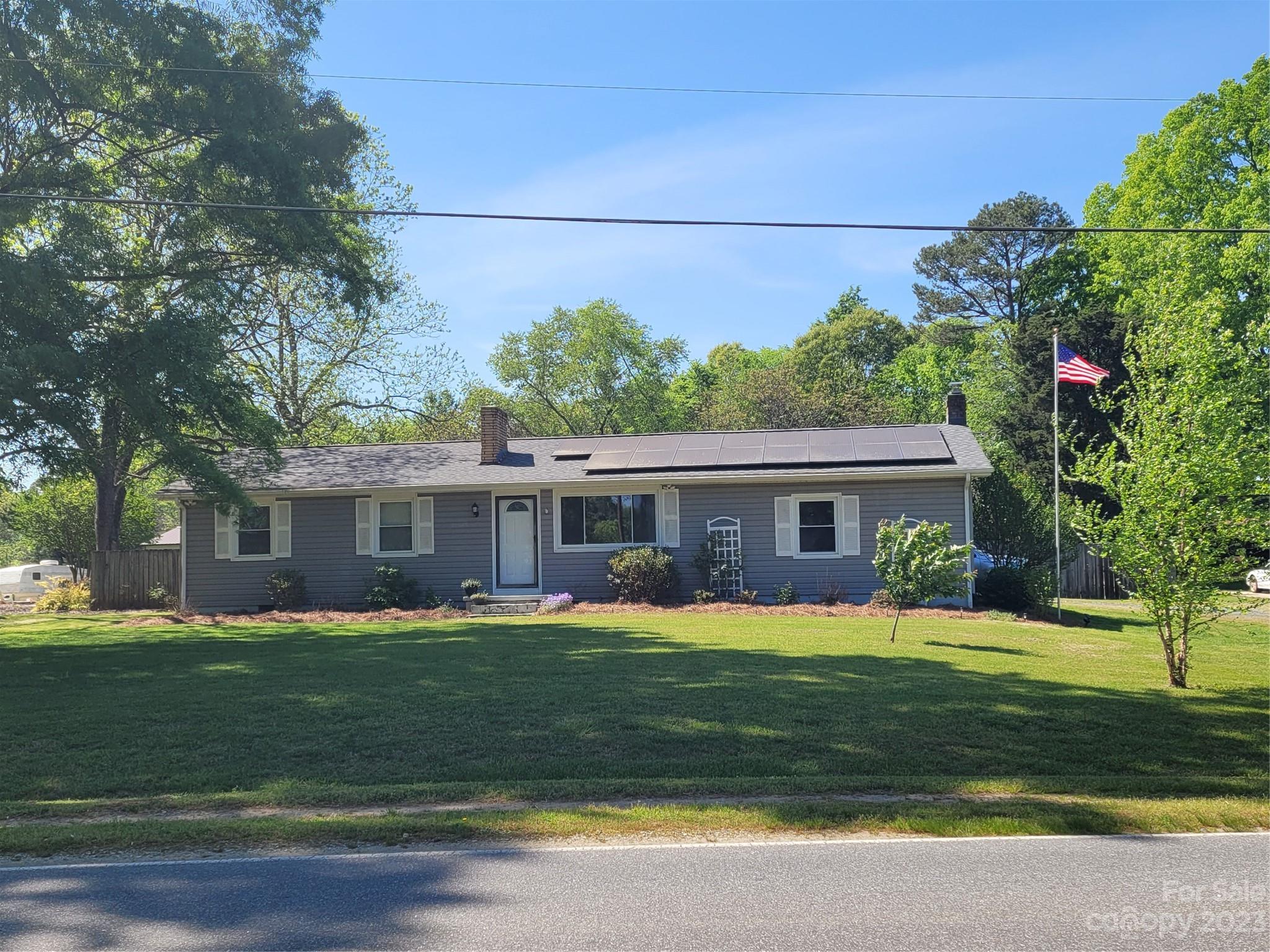 a view of a house with a big yard and potted plants and large trees