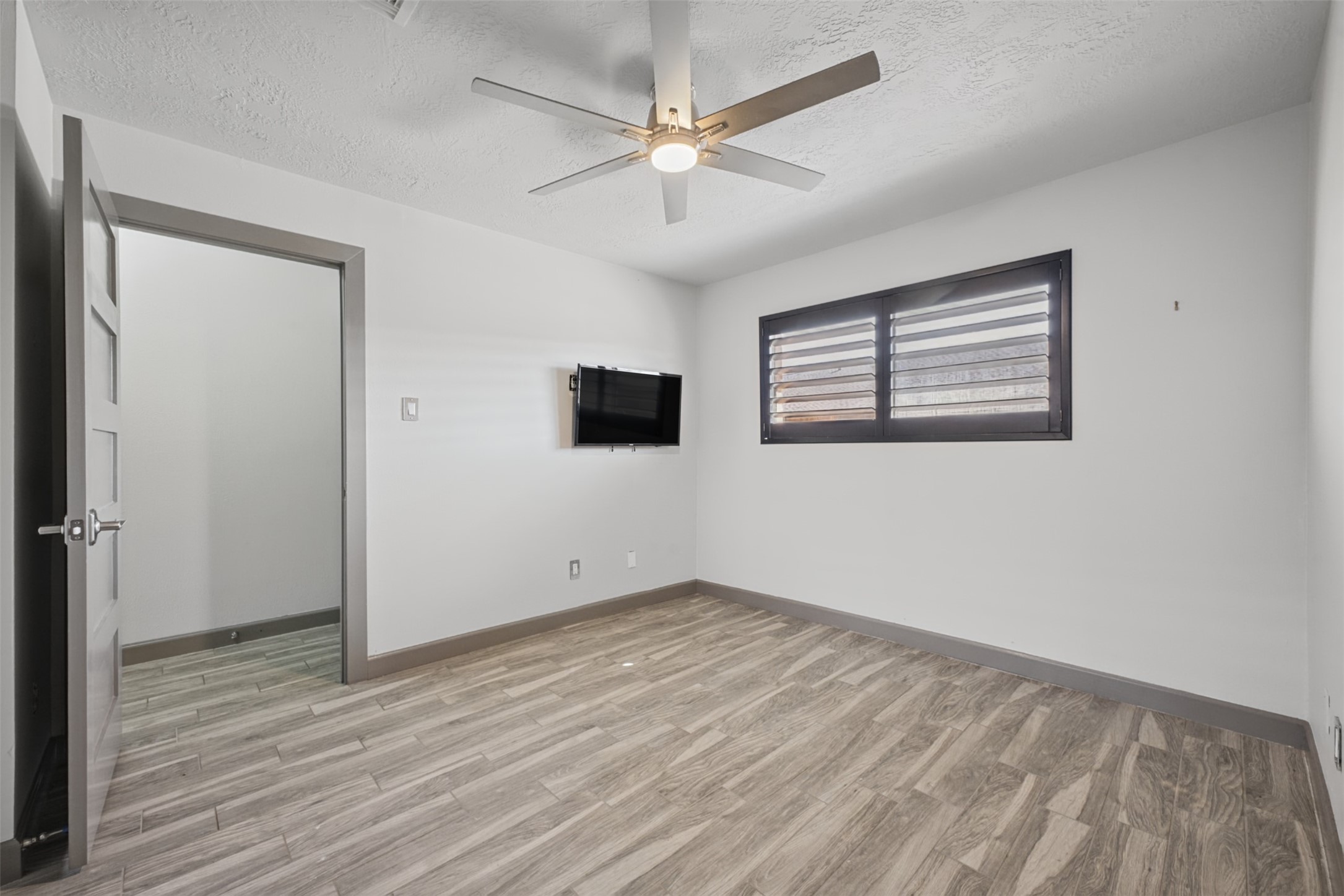 801 River Road, Unit 112F Montgomery, TX 77356 - Photo 15 of 27 Another view of the bedroom highlights the wood-look flooring, contemporary ceiling fan, plantation shutters, and neutral finishes. The wall-mounted TV is included, adding to the move-in-ready convenience.