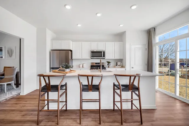 a kitchen with stainless steel appliances kitchen island granite countertop a dining table chairs and a refrigerator