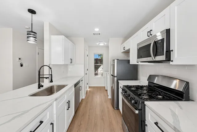 a kitchen with stainless steel appliances granite countertop a stove top oven a sink a refrigerator and white cabinets with wooden floor