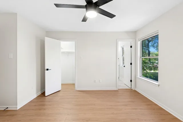 an empty room with wooden floor chandelier fan and windows