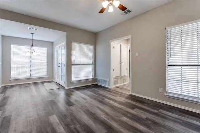 an empty room with wooden floor chandelier and windows
