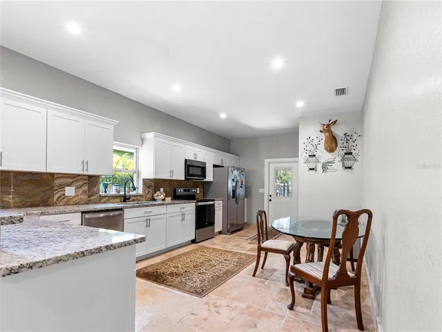 a kitchen with stainless steel appliances granite countertop a stove top oven a sink a dining table and chairs