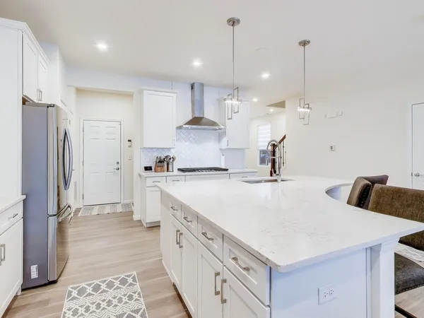 a large white kitchen with a stove a sink a refrigerator and white cabinets with wooden floor